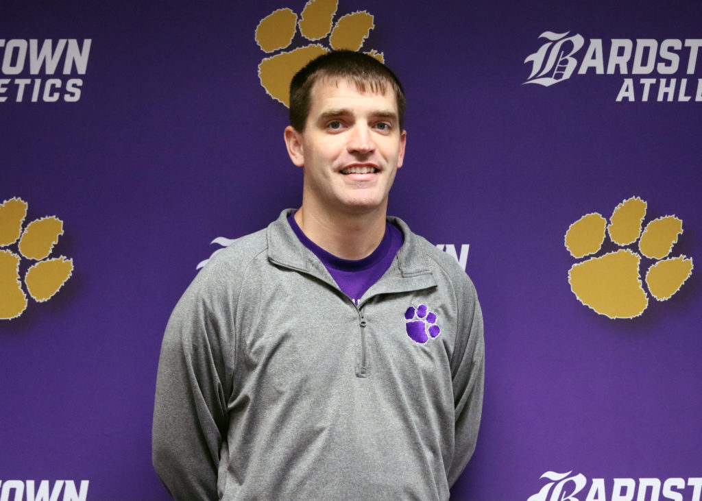 Darren Morris, head volleyball coach, stands in front of a banner.